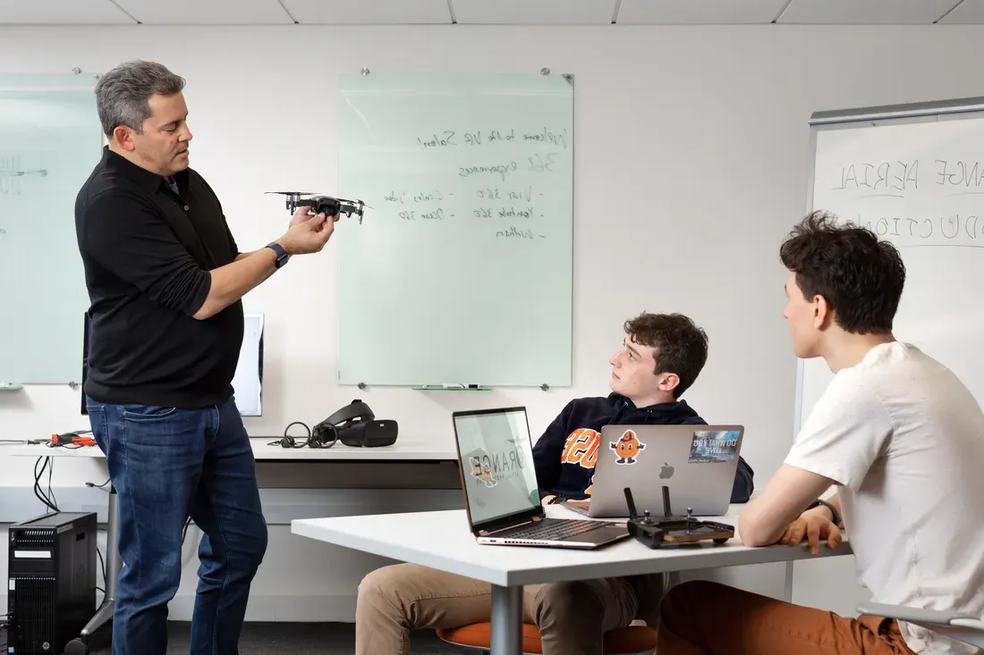 Professor Dan Pacheco working with students in class, holding a drone in his hands.